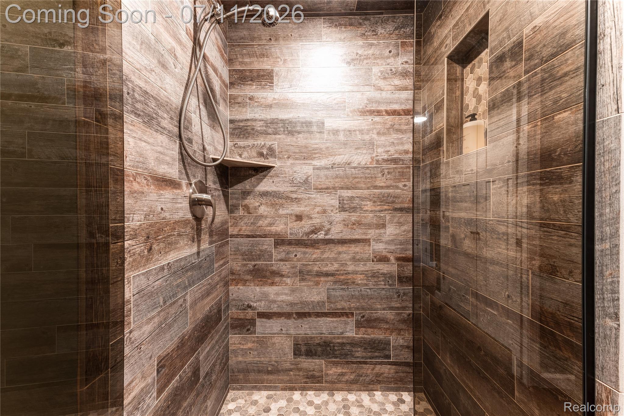 12033 Torrey Road Fenton, MI 48430 - Photo 39 of 51 Walk-in shower featuring wood-look tile walls, a handheld shower fixture, a built-in shower niche with mosaic tile backing, a corner shelf, and a hexagonal tile floor