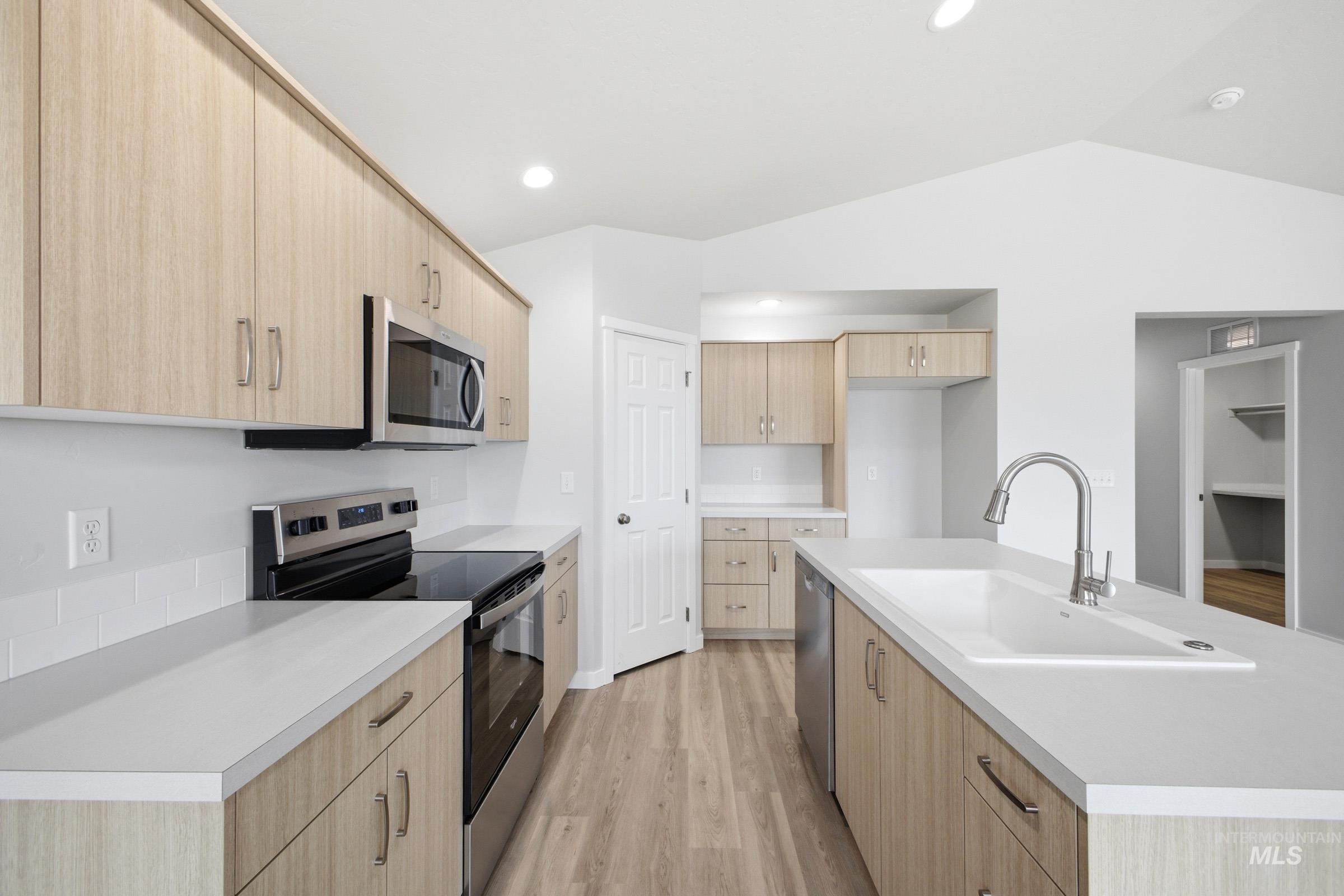 1598 Sunday River Street Middleton, ID 83644 - Photo 5 of 17 Modern kitchen featuring light wood-finish cabinetry, stainless steel appliances, a center island with an integrated sink, white countertops, and wood-finish flooring