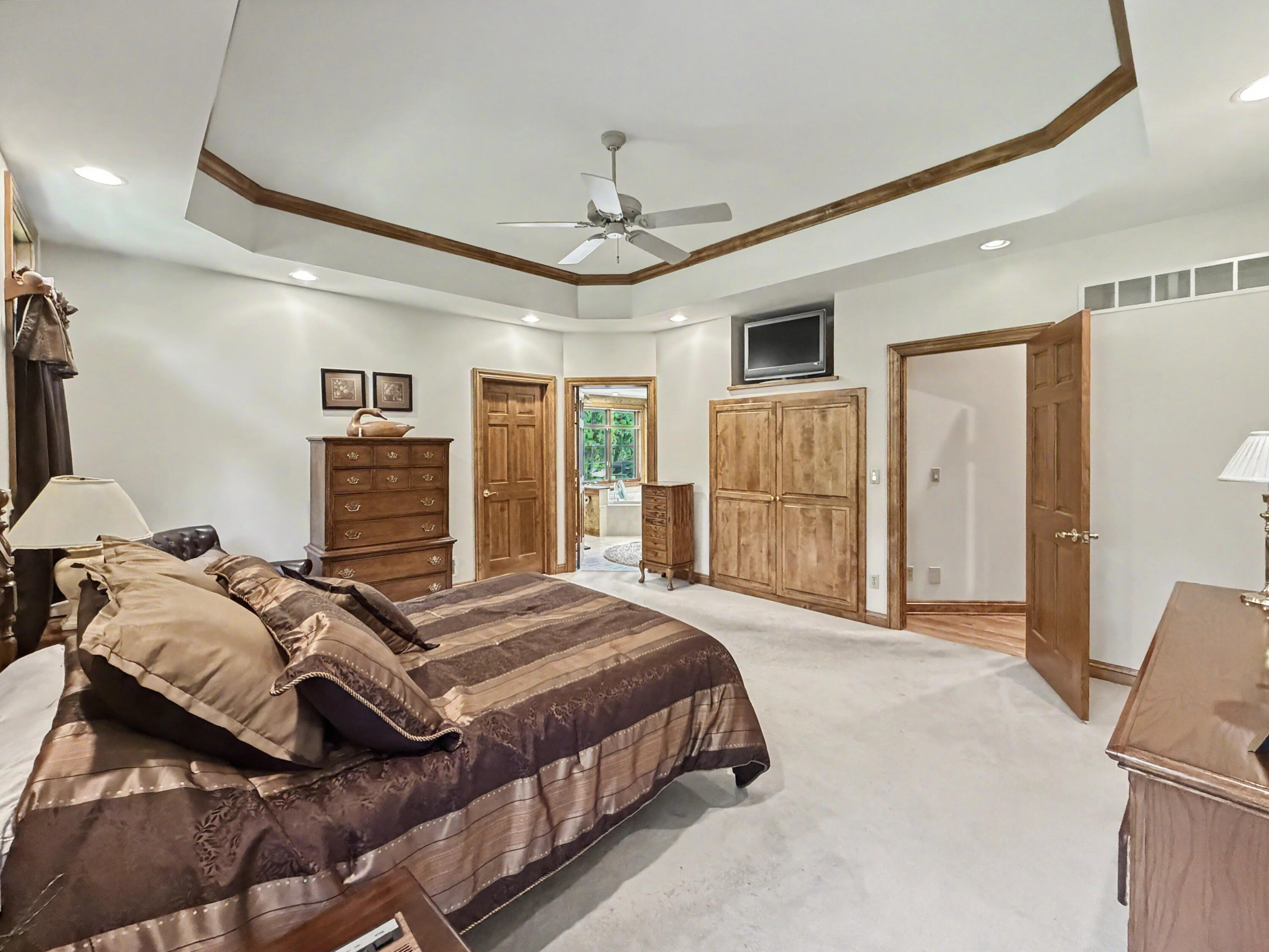 W291-s5245 Ridgefield Road Waukesha, WI 53189 - Photo 20 of 44 The expansive primary suite offers a stunning tray ceiling, serene wooded views, and generous space for furnishings and relaxation. The luxurious ensuite bath features a whirlpool soaking tub, oversized walk-in shower, dual-sink vanity, and spacious walk-in closet, creating a true private retreat.