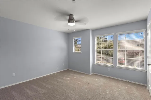 an empty room with chandelier fan and windows