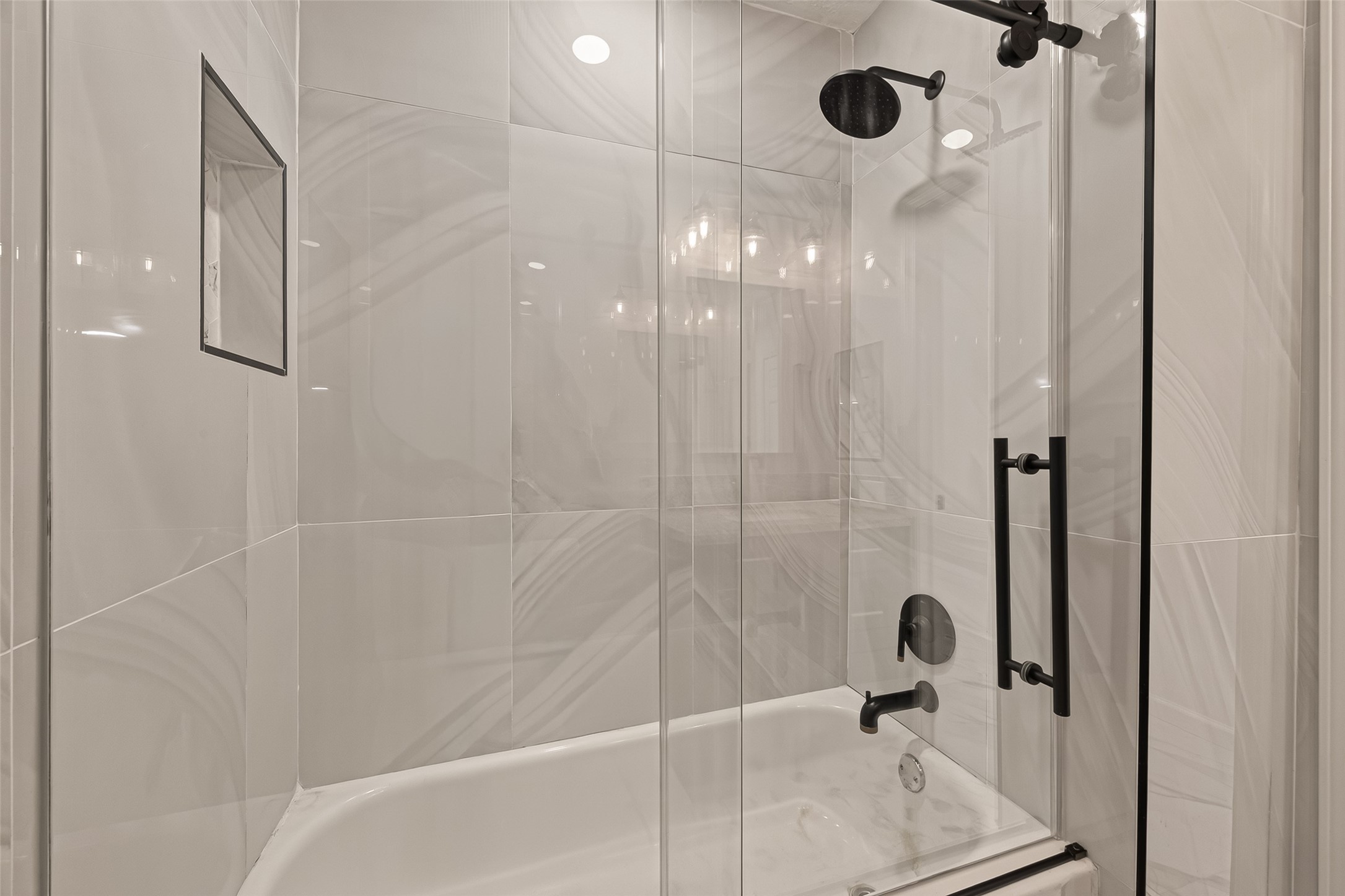 16619 Tibet Road Friendswood, TX 77546 - Photo 20 of 29 This bathroom features a modern shower with sleek glass doors, elegant tile walls, and a built-in shelf for convenience. The fixtures are contemporary, adding a stylish touch to the space.