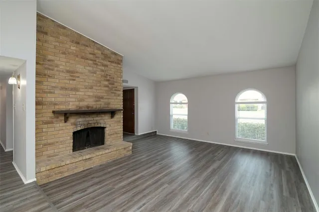 an empty room with wooden floor fireplace and windows