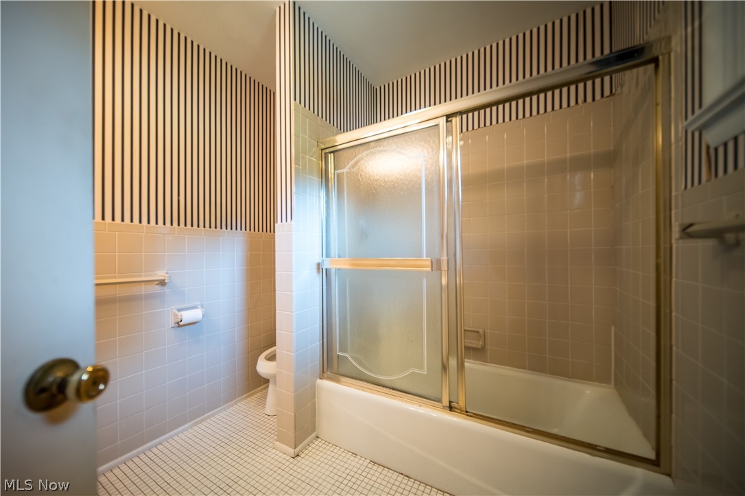 11063 Diagonal Road Mantua, OH 44255 - Photo 21 of 40 Bathroom with tile walls, tile patterned floors, toilet, and shower / bath combination with glass door