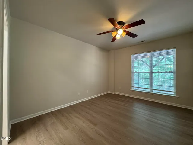 an empty room with wooden floor fan and windows