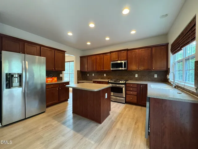 a kitchen with stainless steel appliances granite countertop a refrigerator a sink dishwasher a stove top oven and a center island with wooden floor