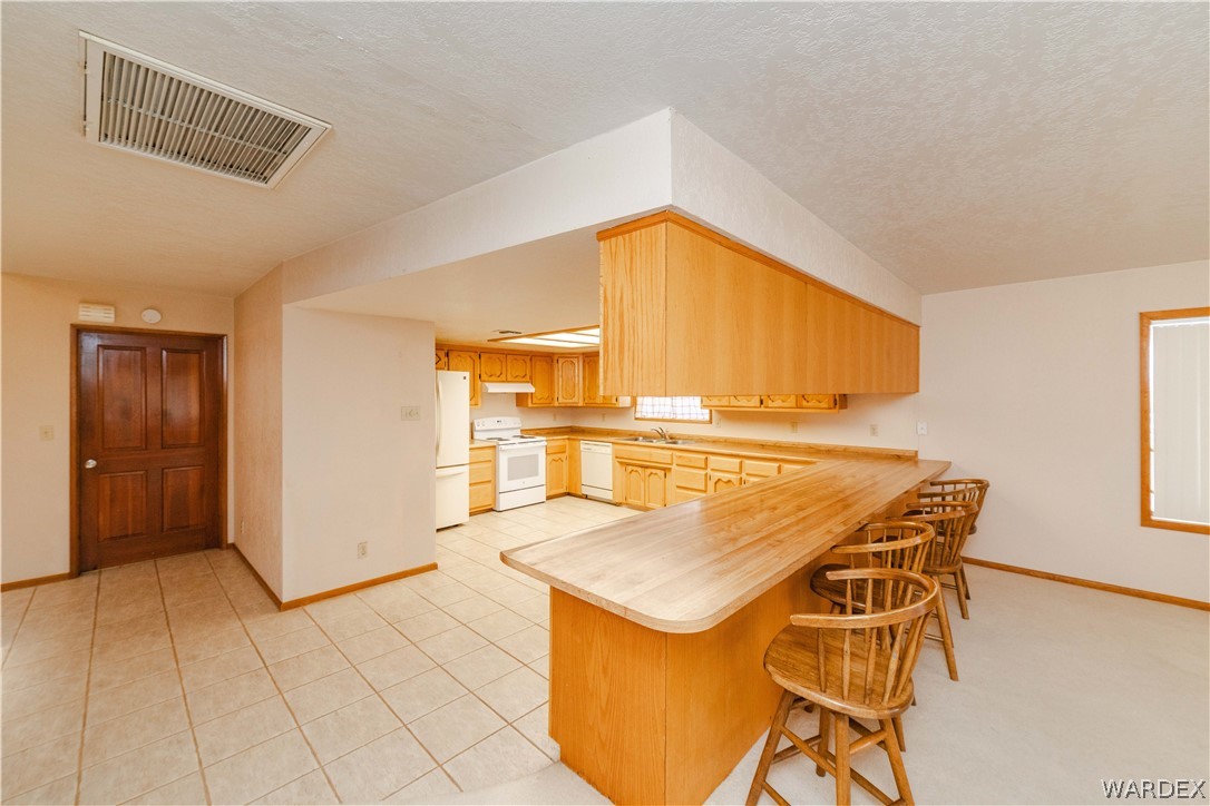 2100 East Valley View Road Kingman, AZ 86409 - Photo 11 of 53 Spacious kitchen featuring a large breakfast bar, wood cabinetry, white appliances, and tiled flooring