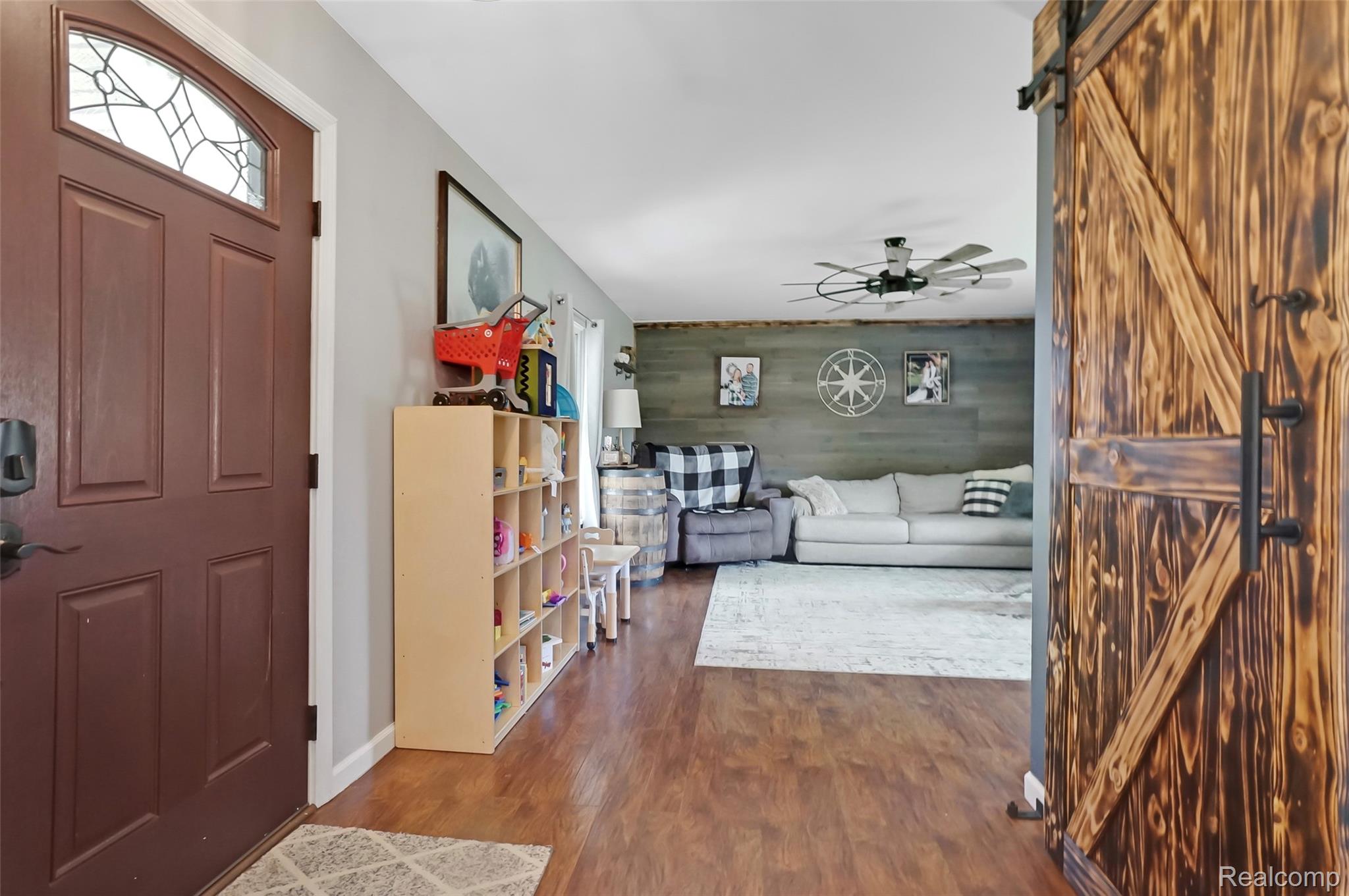 6050 Brophy Road Howell, MI 48855 - Photo 3 of 27 Wood-finish flooring throughout, featuring a rich, dark barn door with black hardware, a panel front door with decorative glass, and a modern ceiling fan