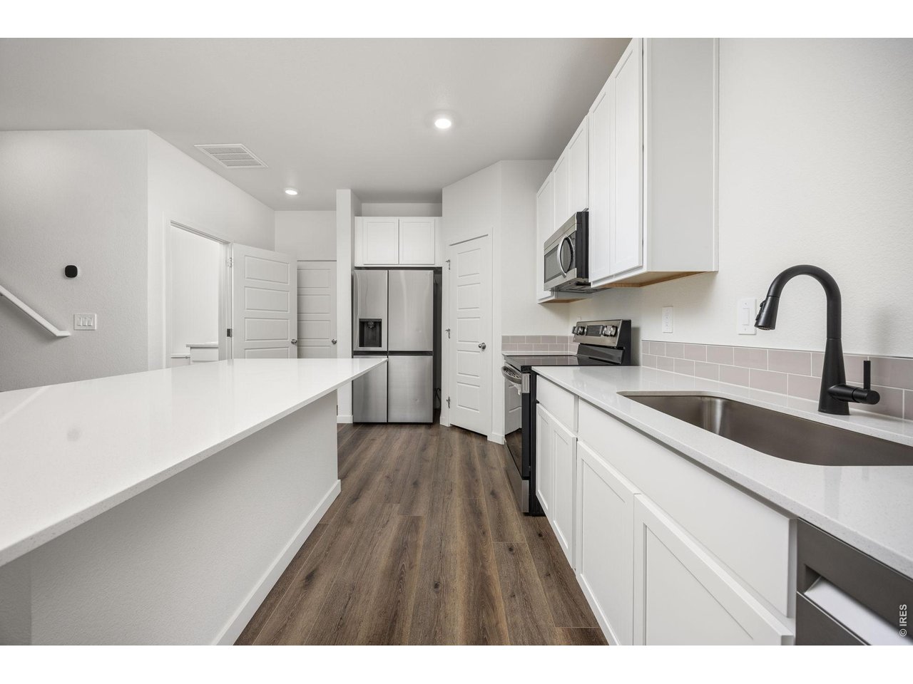 315 Condor Way Johnstown, CO 80534 - Photo 9 of 25 a kitchen with stainless steel appliances a sink dishwasher a refrigerator and white cabinets with wooden floor