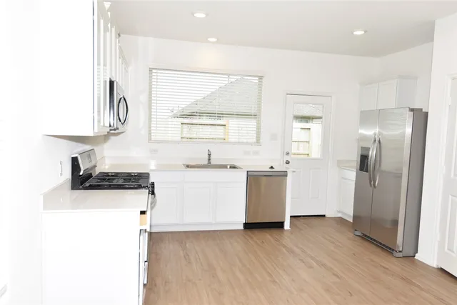 a kitchen with a sink a refrigerator a stove and white cabinets with wooden floor