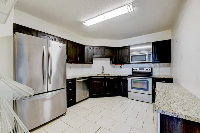 a kitchen with stainless steel appliances granite countertop a stove top oven a sink and a refrigerator