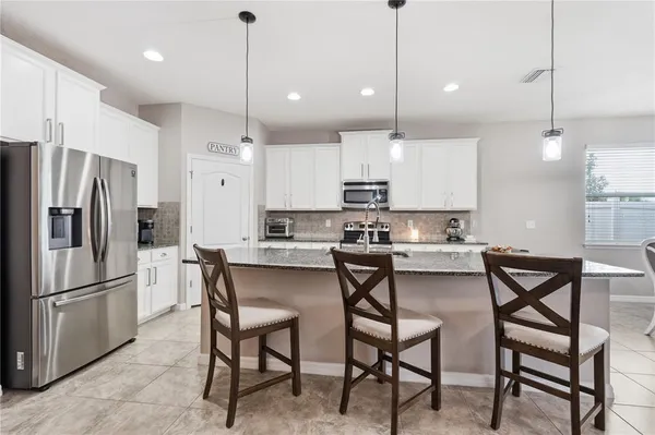 a kitchen with kitchen island a dining table chairs wooden cabinets and refrigerator