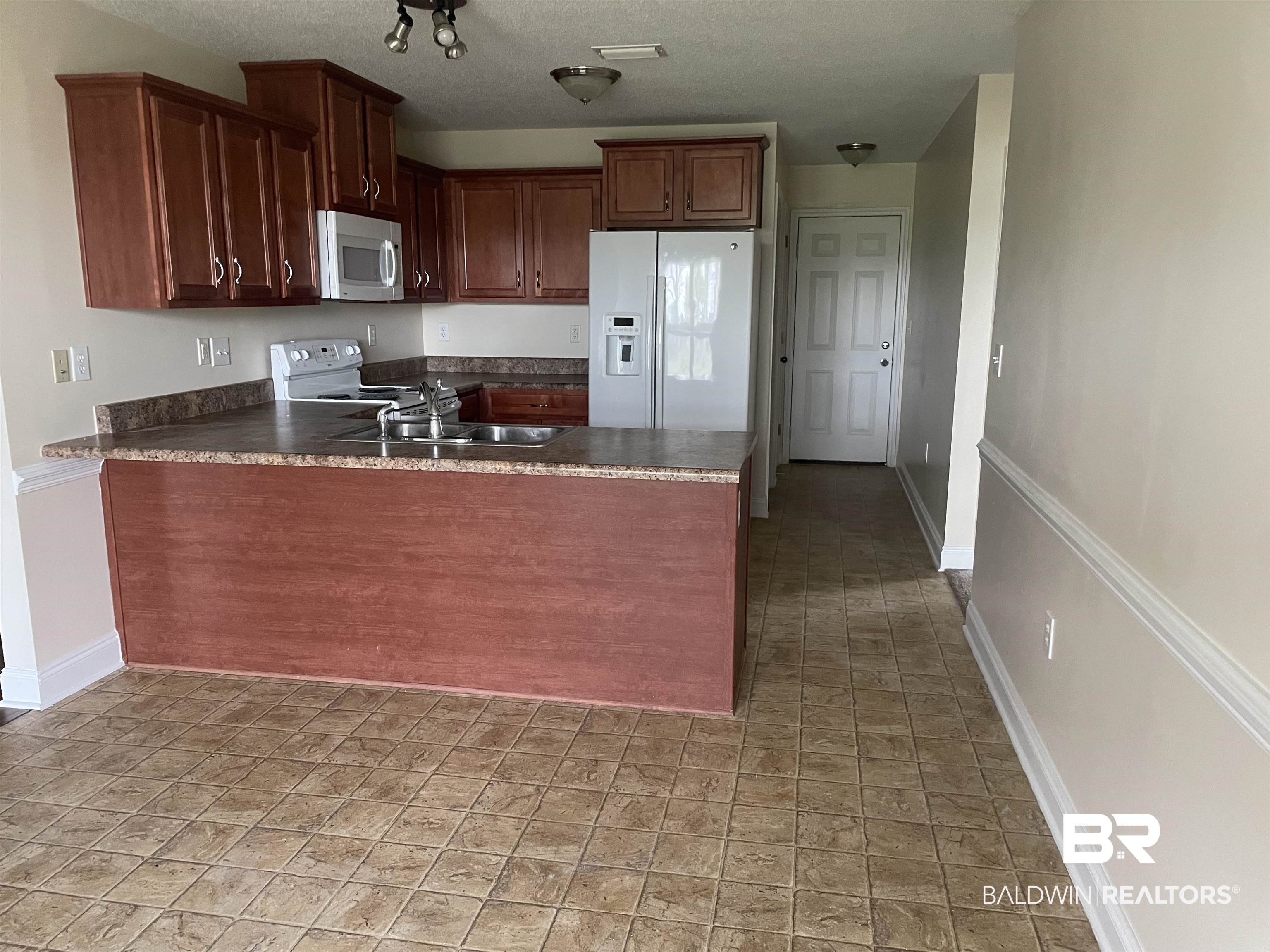 23575 Fountain Street Robertsdale, AL 36567 - Photo 19 of 19 Kitchen featuring dark countertops, a sink, white appliances, a peninsula, and baseboards