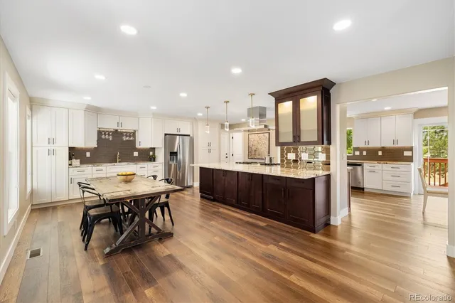 a kitchen with stainless steel appliances kitchen island granite countertop a refrigerator a stove a sink a dining table and chairs with wooden floor