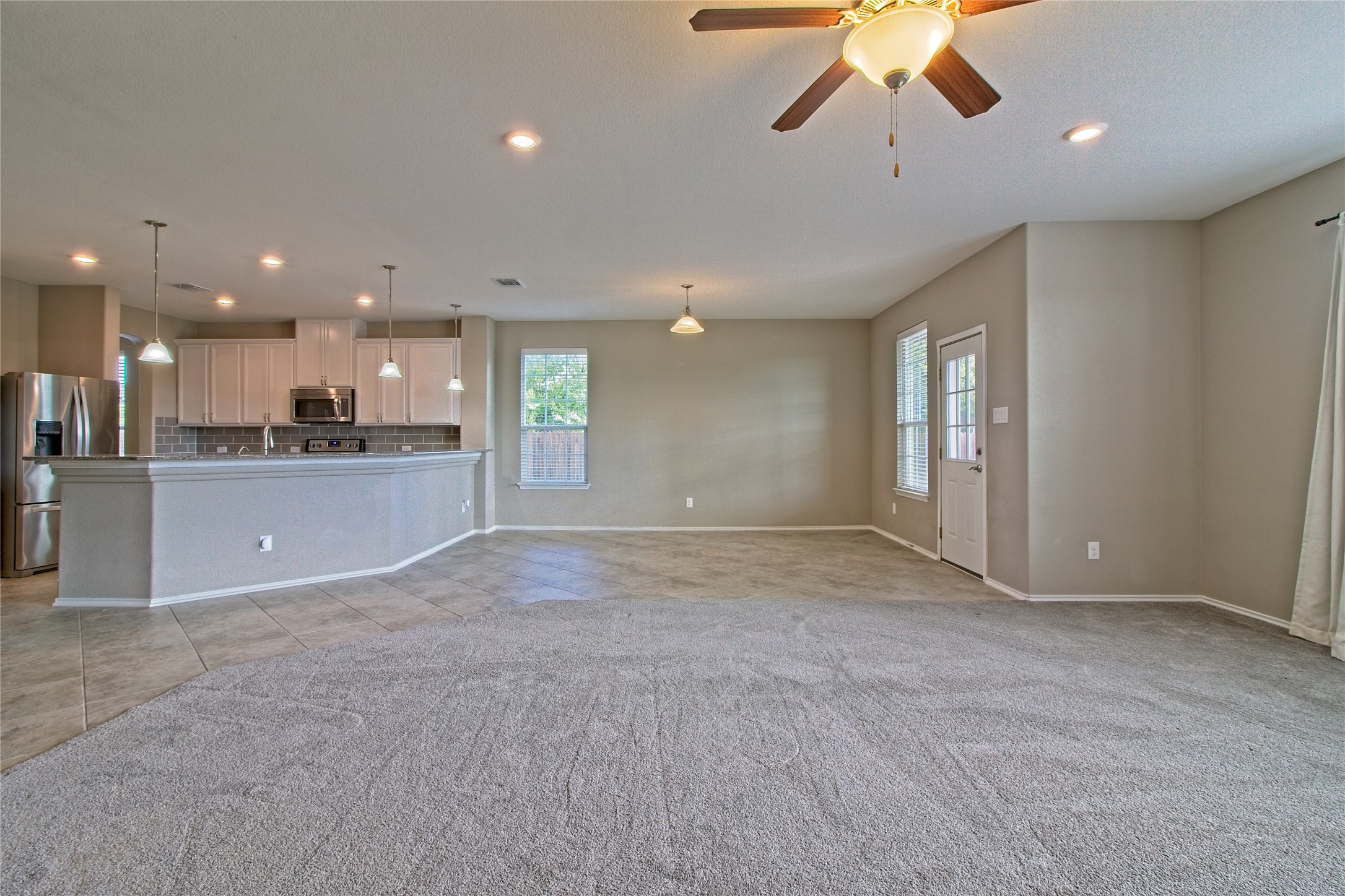 31443 Kingsway Road Georgetown, TX 78628 - Photo 10 of 40 An open-concept living area boasts a modern kitchen with a breakfast bar, seamlessly flowing into a carpeted family room.
