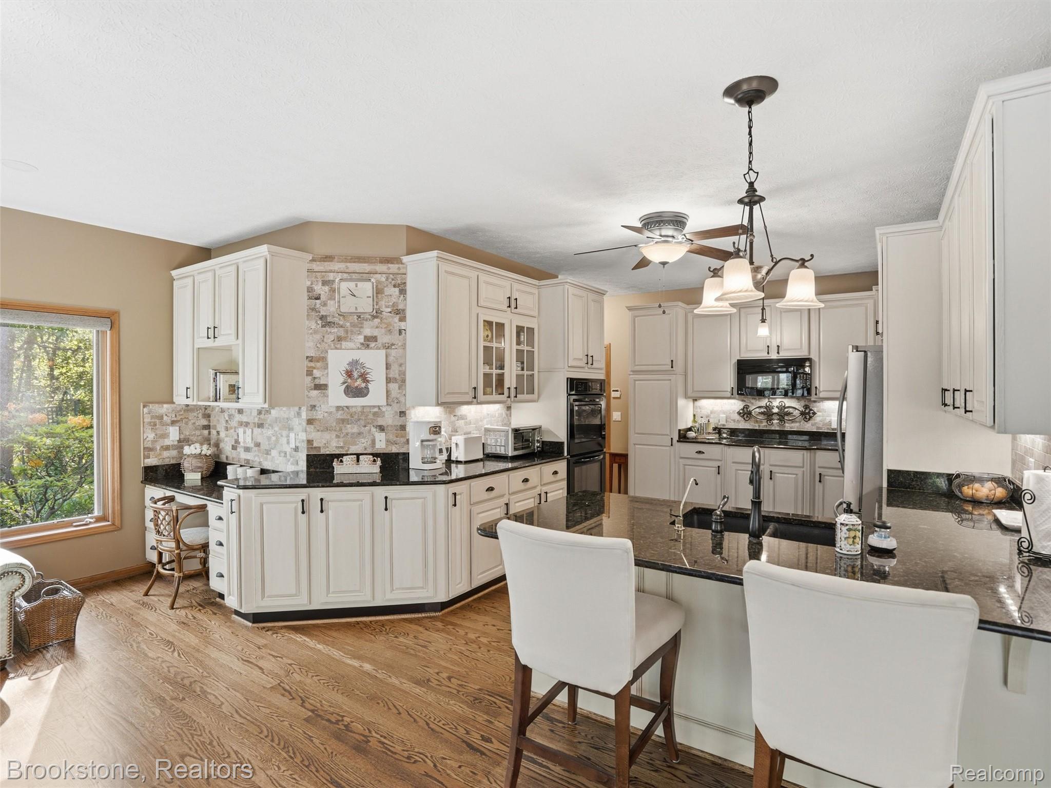9523 Quail Ridge Run Brighton, MI 48114 - Photo 17 of 50 Open-concept kitchen with white cabinetry, black countertops, wood-finish flooring, a built-in desk area, and a central island with bar seating
