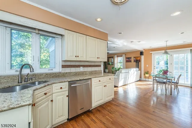 a kitchen with stainless steel appliances granite countertop a stove a sink dishwasher and white cabinets with wooden floor