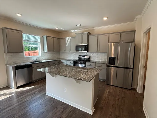 a kitchen with kitchen island granite countertop stainless steel appliances a refrigerator a sink a stove a microwave a center island and a window