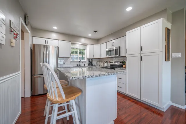 a kitchen with stainless steel appliances granite countertop a refrigerator a microwave oven a sink dishwasher and white cabinets with wooden floor