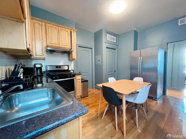 a kitchen with stainless steel appliances granite countertop a stove a refrigerator a sink a dining table and chairs with wooden floor