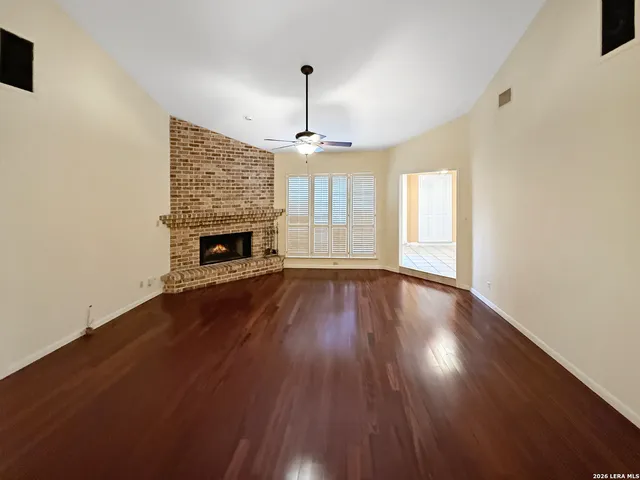 an empty room with wooden floor fireplace and windows