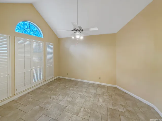 an empty room with chandelier fan and windows