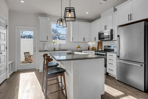 a kitchen with stainless steel appliances granite countertop a stove top oven a refrigerator a sink a dining table and chairs with wooden floor