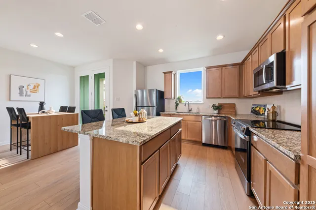 a kitchen with stainless steel appliances granite countertop a stove top oven a sink dishwasher a refrigerator and a dining table with wooden floor
