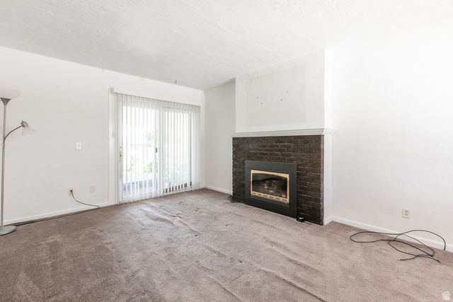 59 East Pinehurst Street Tooele, UT 84074 - Photo 4 of 22 Living area featuring a dark brick fireplace with a white mantel, sliding glass door with vertical blinds, and neutral carpet flooring