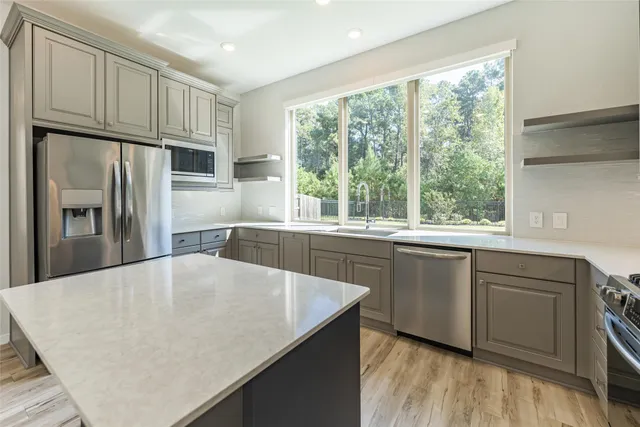 a kitchen with stainless steel appliances granite countertop a refrigerator a sink dishwasher a stove and white countertops with wooden floor