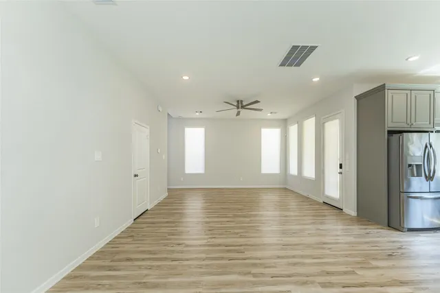 a view of an empty room with wooden floor and a kitchen