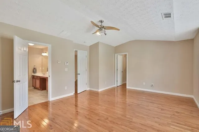 a view of an empty room with wooden floor and a ceiling fan