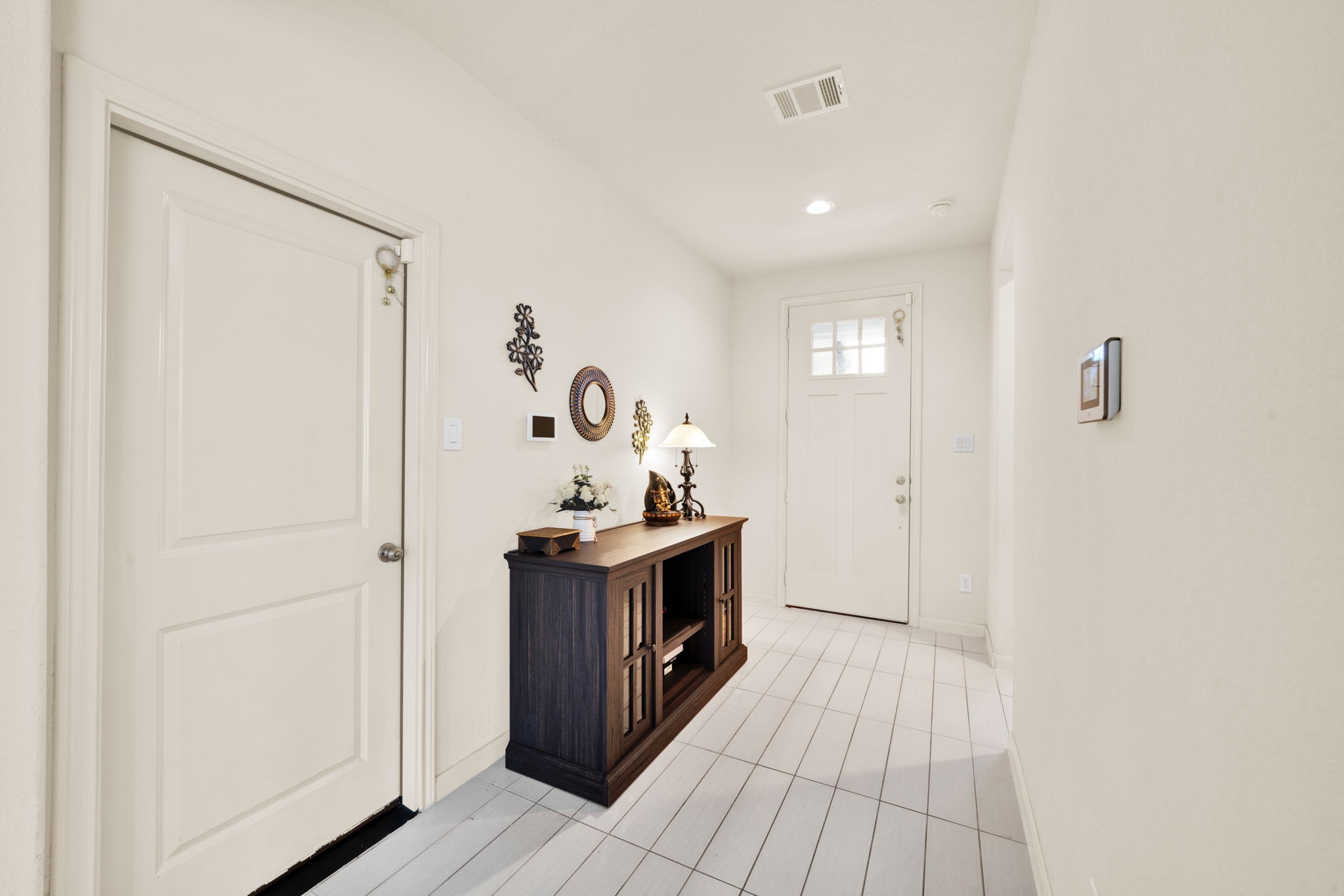 2503 Hagerman Road Conroe, TX 77384 - Photo 15 of 43 Bright entryway with light-colored walls and tiled floor. Features a wooden console table with decorative items, wall accents, and a door with a window panel, offering a welcoming atmosphere.