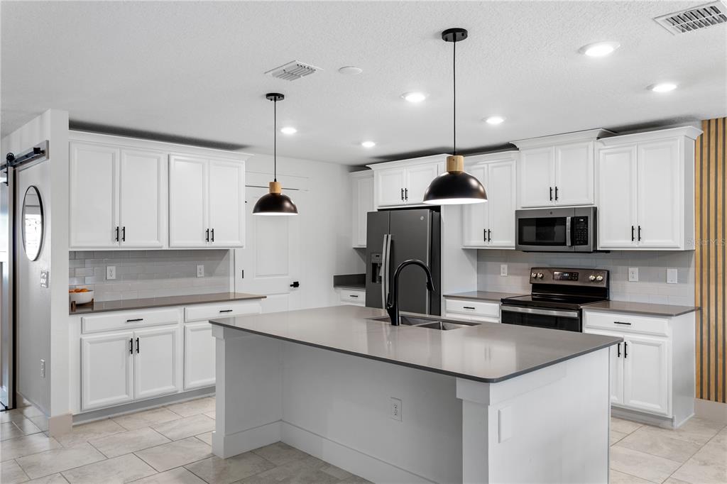 5693 Alenlon Way Mount Dora, FL 32757 - Photo 9 of 40 a kitchen with kitchen island granite countertop a sink a center island stainless steel appliances and cabinets