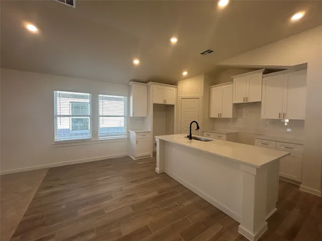 a large white kitchen with kitchen island a sink wooden floor and a large window