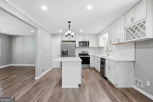 a kitchen with granite countertop a refrigerator oven a sink dishwasher and white cabinets with wooden floor