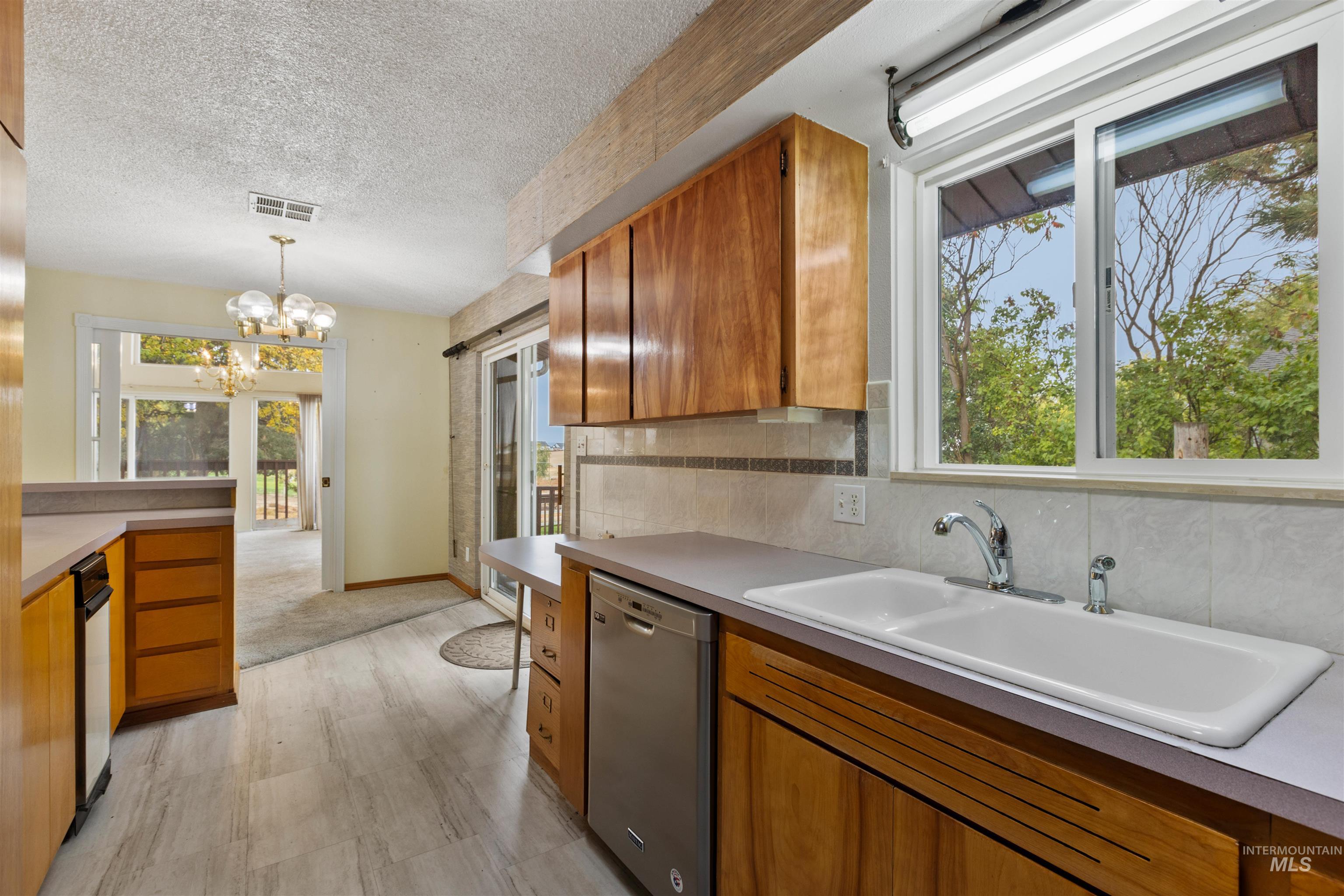 9948 Ash Lane Payette, ID 83661 - Photo 15 of 34 Kitchen featuring brown cabinetry, dishwasher, decorative light fixtures, decorative backsplash, and a textured ceiling