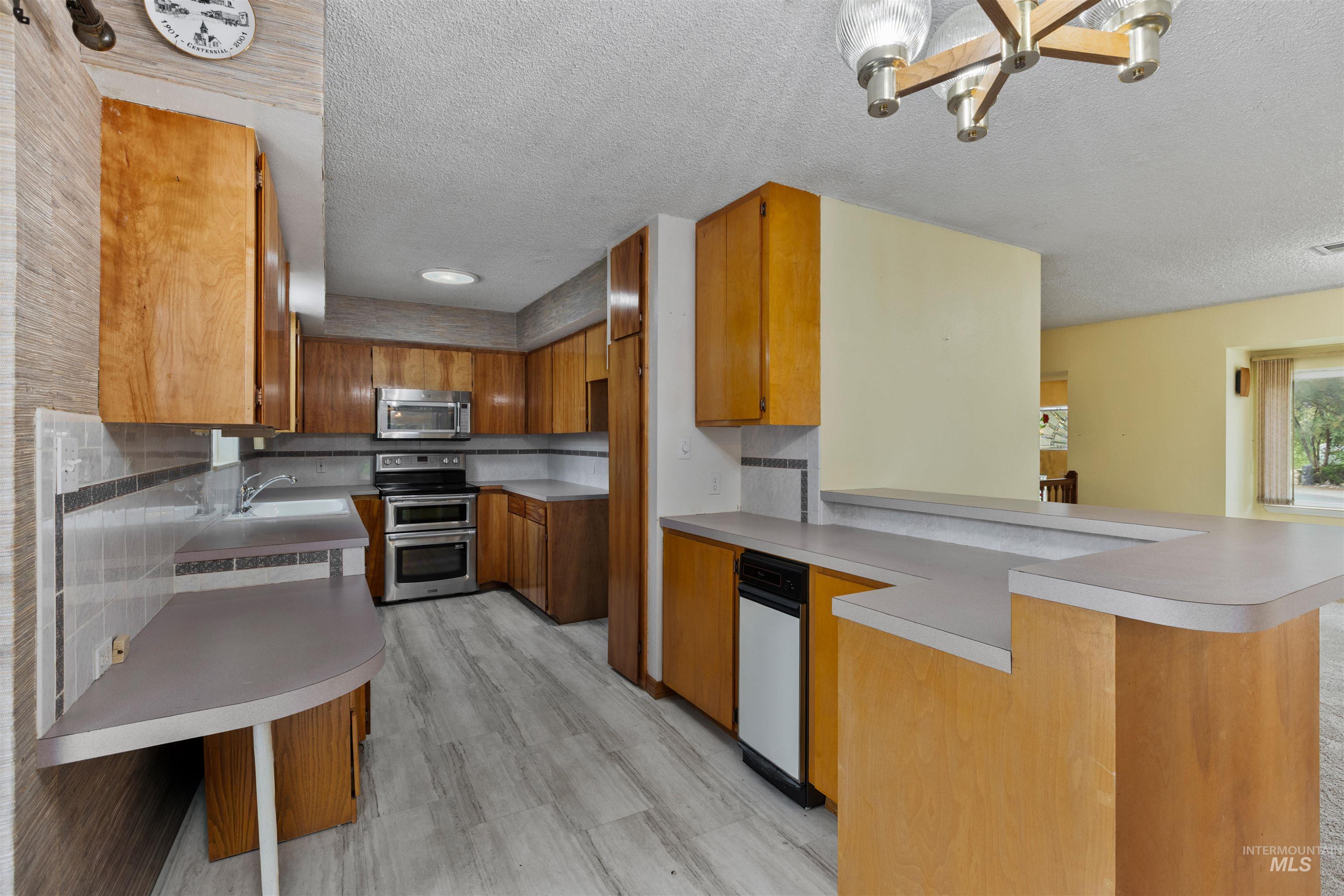 9948 Ash Lane Payette, ID 83661 - Photo 16 of 34 Kitchen with brown cabinetry, a textured ceiling, light countertops, appliances with stainless steel finishes, and a peninsula