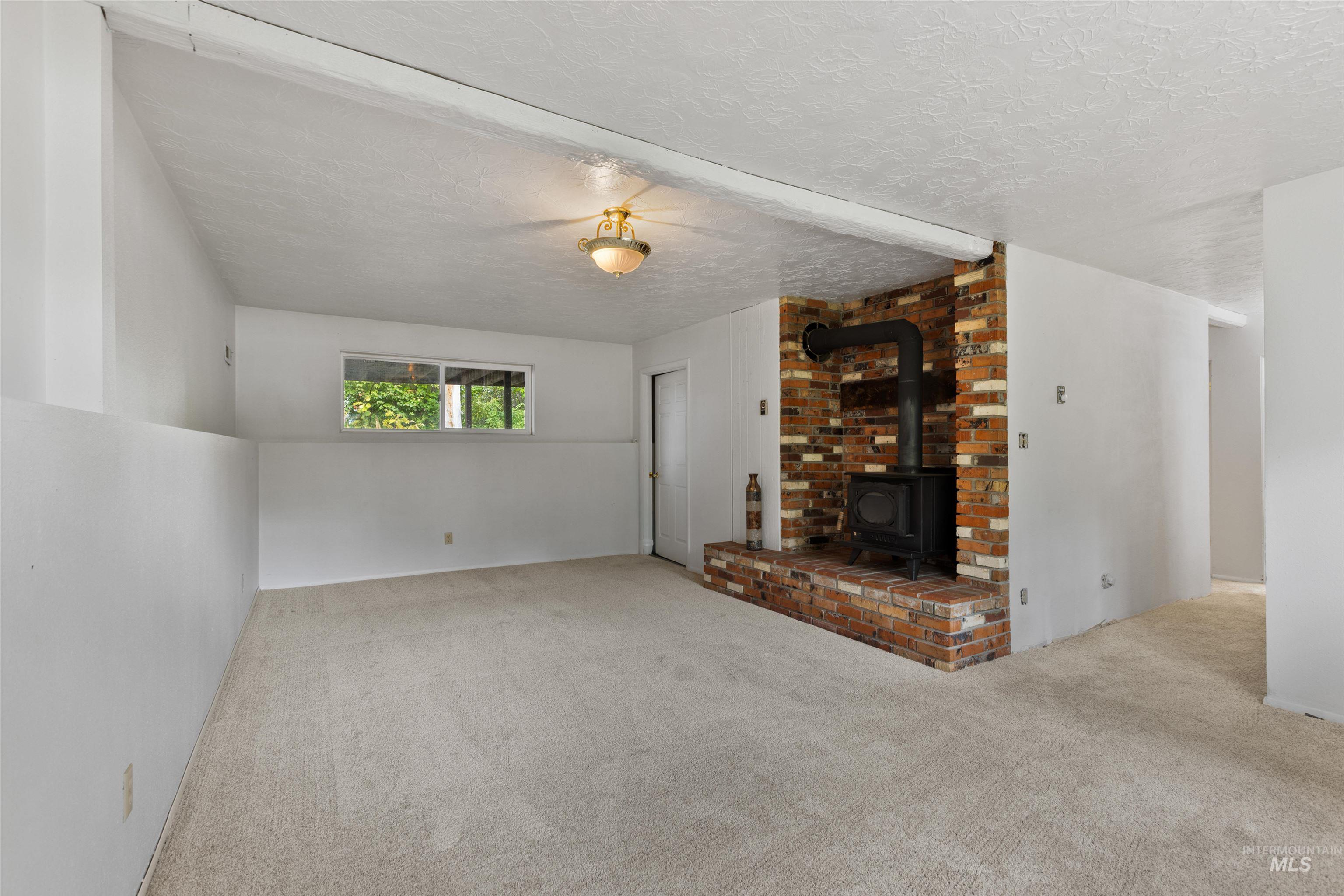 9948 Ash Lane Payette, ID 83661 - Photo 25 of 34 Unfurnished living room with a wood stove, carpet floors, and a textured ceiling