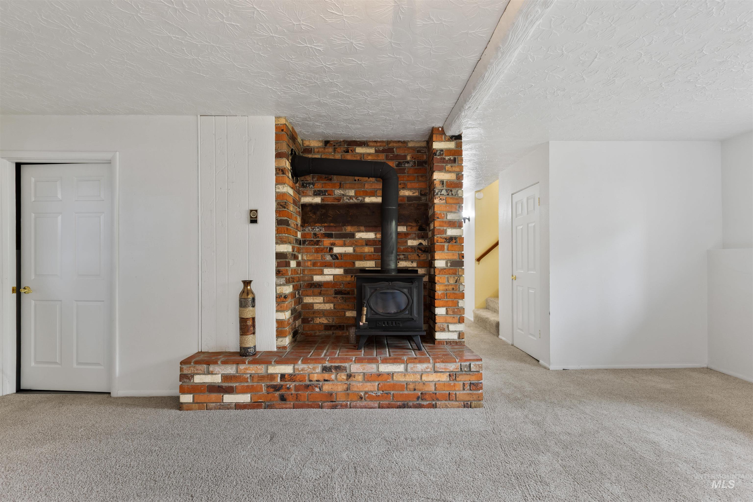 9948 Ash Lane Payette, ID 83661 - Photo 26 of 34 Unfurnished living room with a wood stove, carpet flooring, stairs, and a textured ceiling