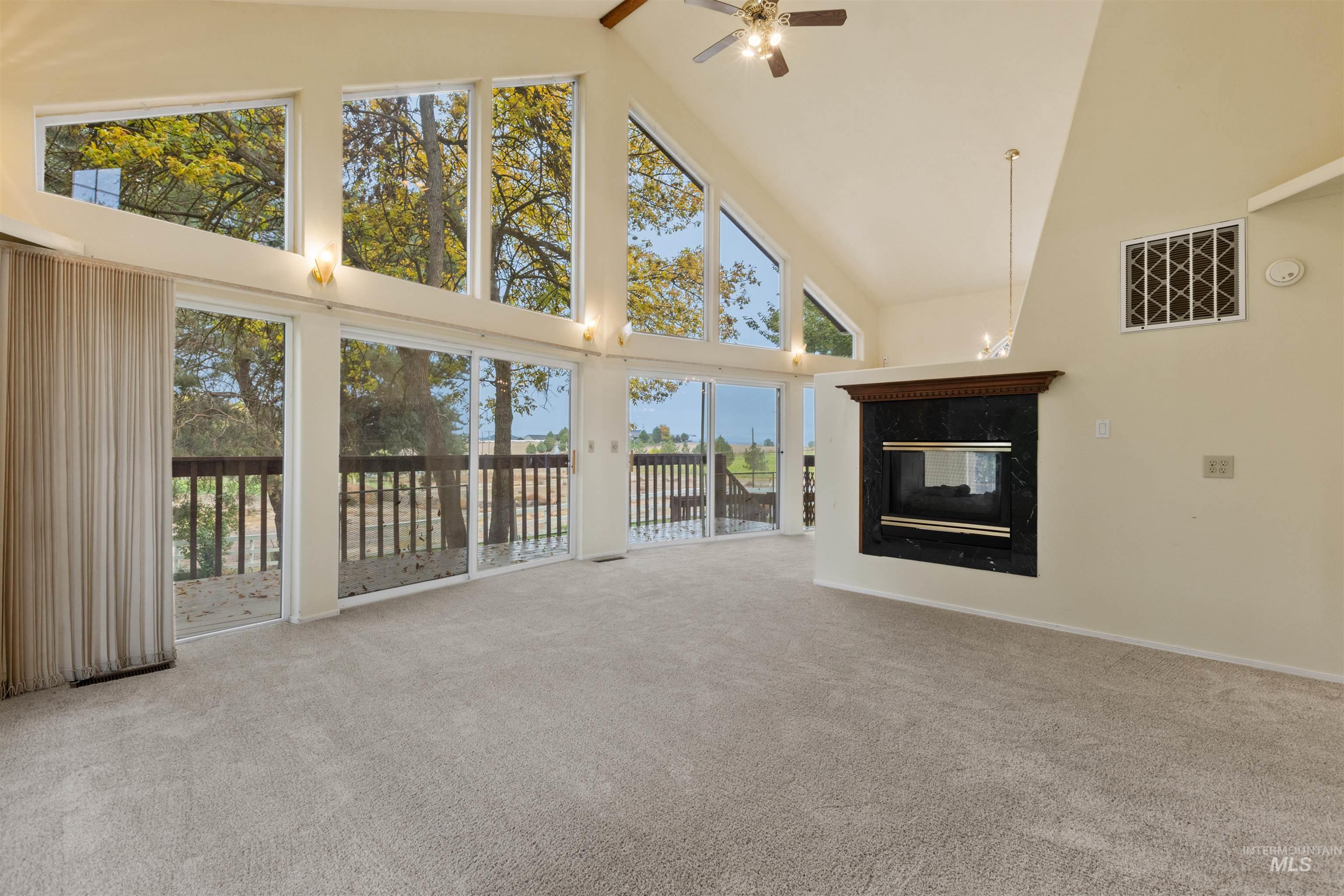 9948 Ash Lane Payette, ID 83661 - Photo 5 of 34 Unfurnished living room with high vaulted ceiling, a multi sided fireplace, light colored carpet, and ceiling fan