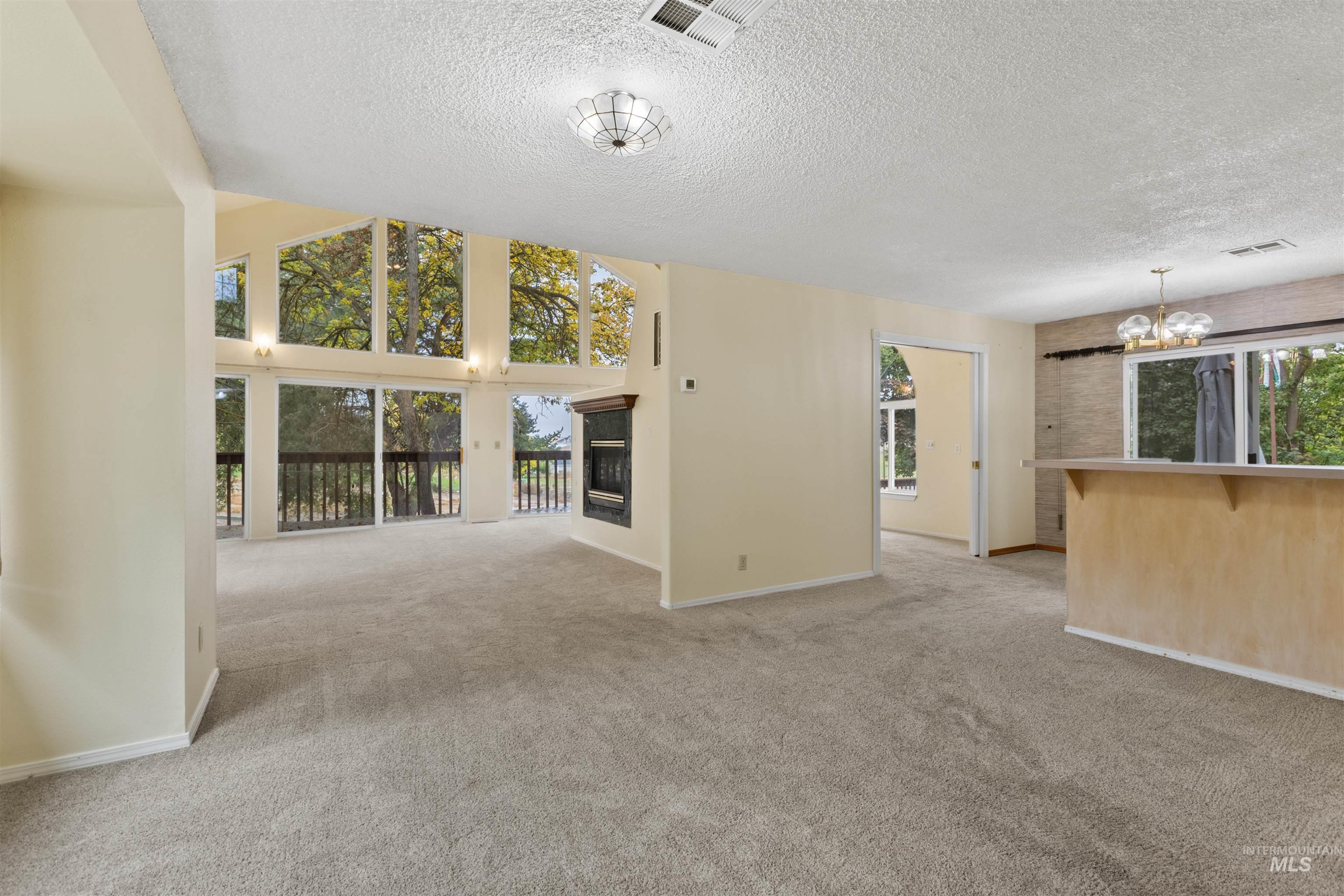 9948 Ash Lane Payette, ID 83661 - Photo 8 of 34 Unfurnished living room with light colored carpet, a chandelier, a glass covered fireplace, a textured ceiling, and a towering ceiling