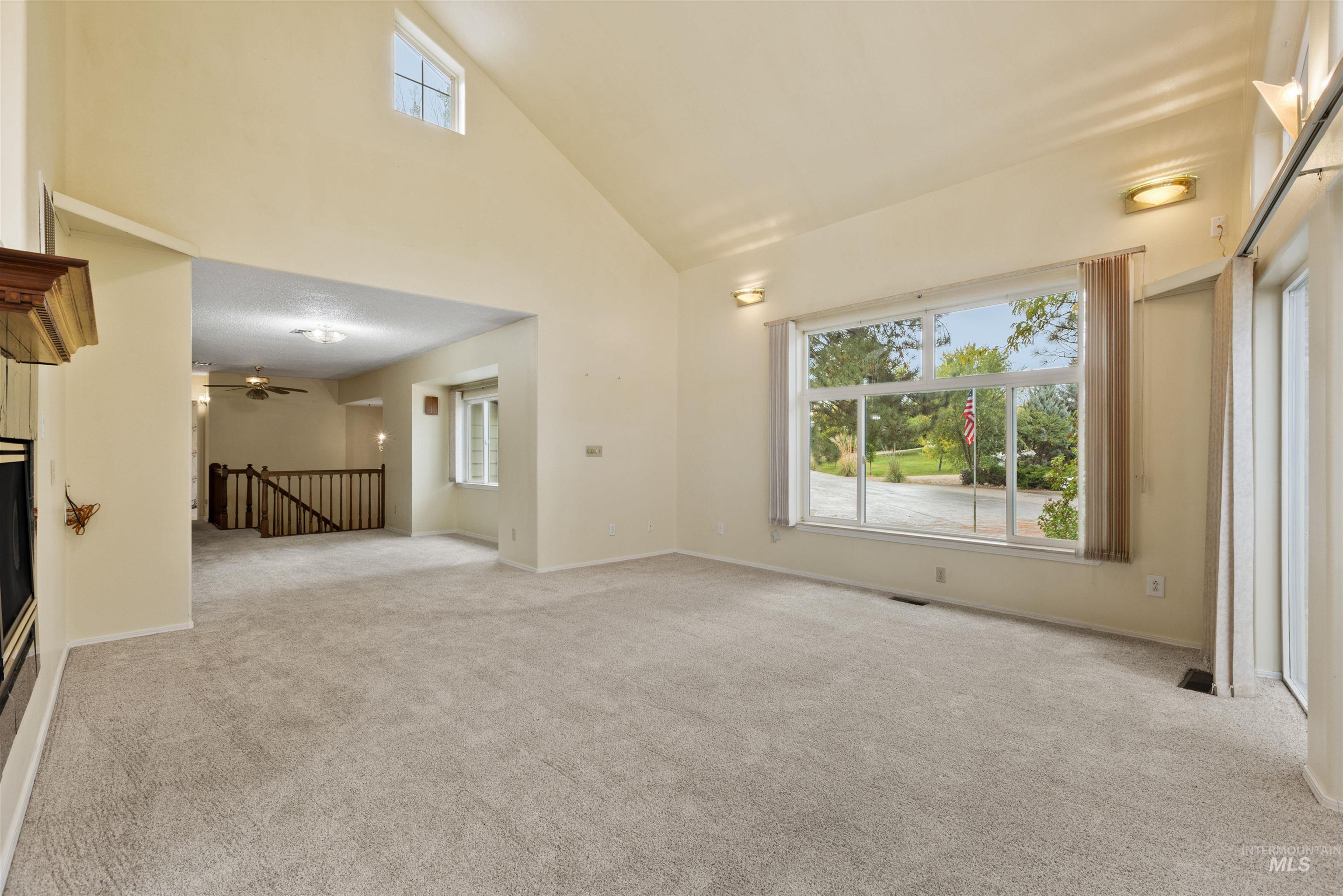 9948 Ash Lane Payette, ID 83661 - Photo 9 of 34 Unfurnished living room with high vaulted ceiling, light carpet, ceiling fan, and a glass covered fireplace