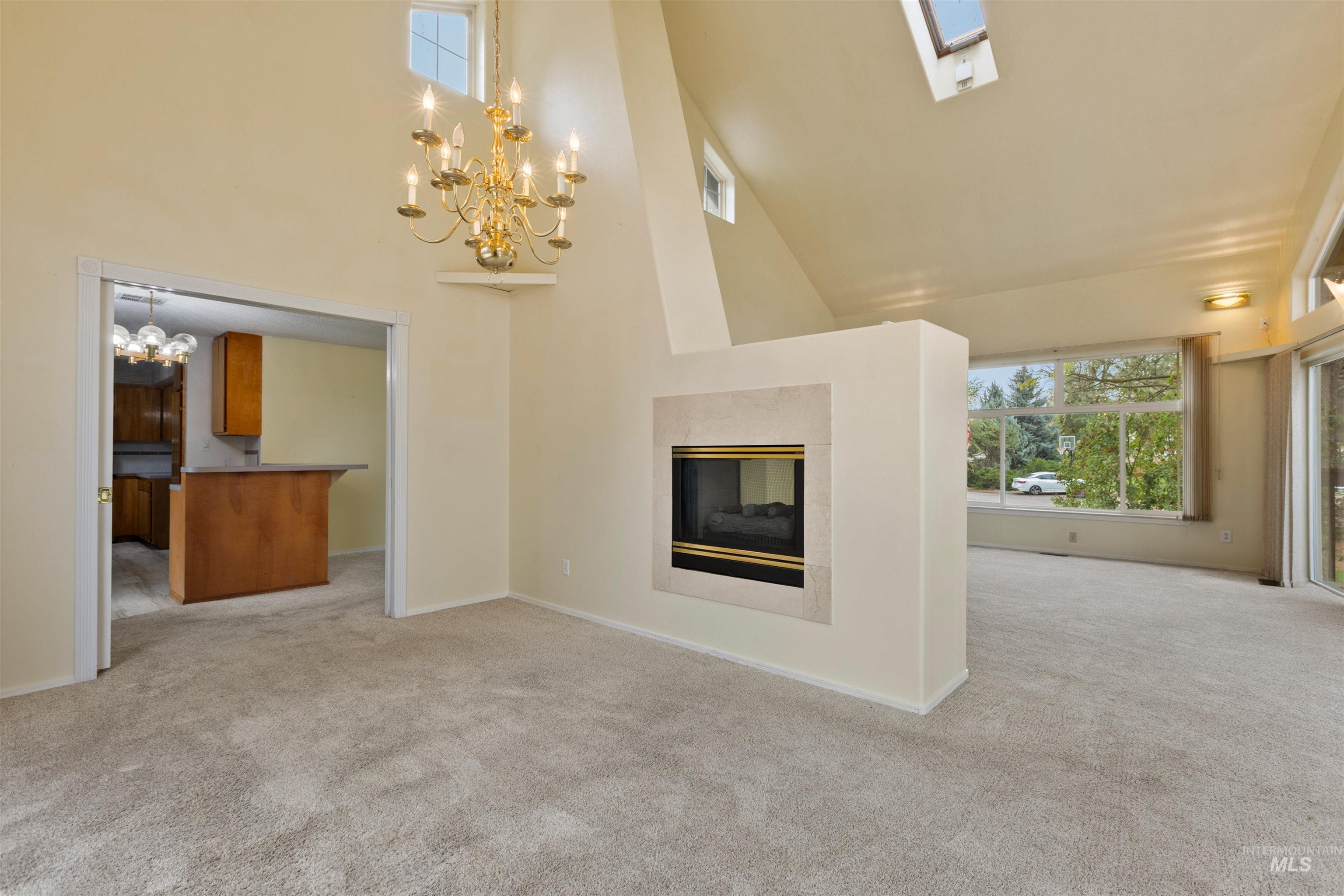 9948 Ash Lane Payette, ID 83661 - Photo 10 of 34 Unfurnished living room with high vaulted ceiling, light colored carpet, a multi sided fireplace, a chandelier, and a skylight