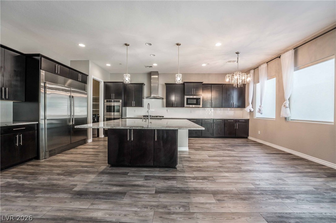 2787 Athens Ridge Drive Henderson, NV 89052 - Photo 7 of 31 An open-concept kitchen features dark cabinetry, integrated appliances, and a central island with a granite countertop, creating a sophisticated culinary space.