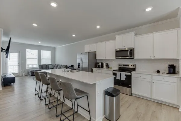 a kitchen with stainless steel appliances kitchen island granite countertop a stove top oven a sink a refrigerator with white cabinets and wooden floor