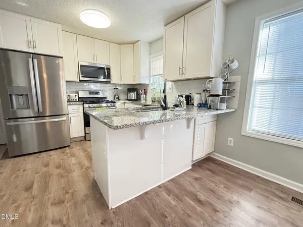 a kitchen with stainless steel appliances granite countertop a stove a sink dishwasher a refrigerator and white cabinets with wooden floor