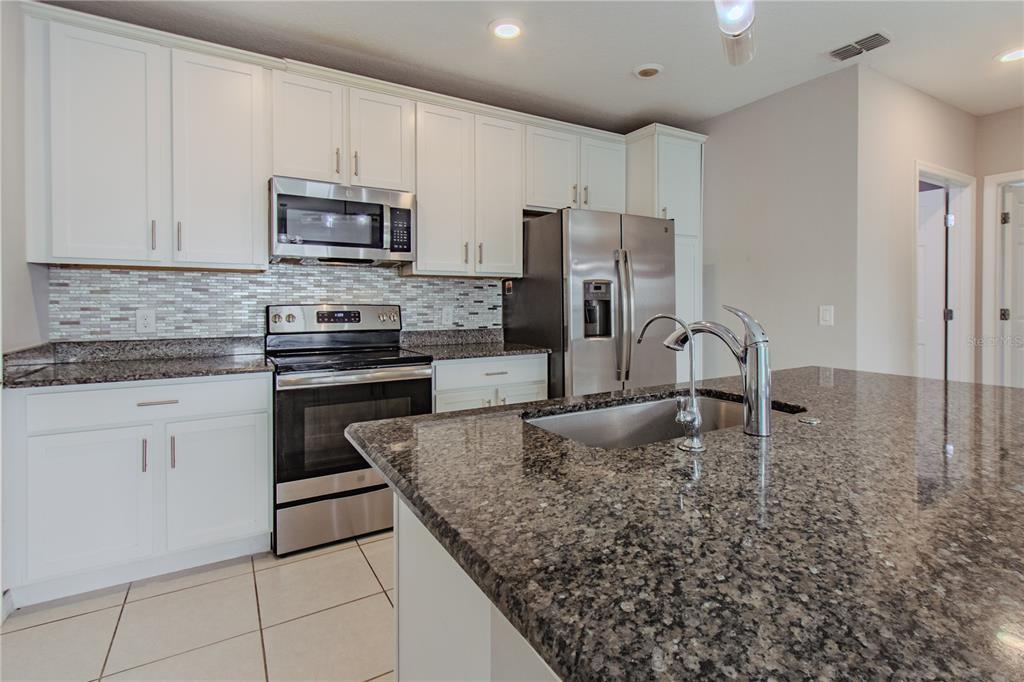 3470 Beau Road Kissimmee, FL 34746 - Photo 7 of 40 a kitchen with kitchen island granite countertop a sink stove and refrigerator