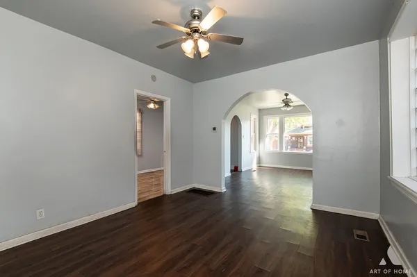 an empty room with wooden floor chandelier fan and windows
