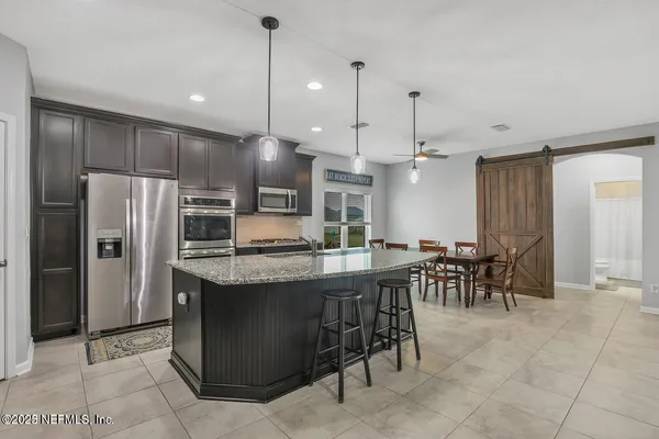 a kitchen with stainless steel appliances kitchen island granite countertop a table a chairs a refrigerator and a sink