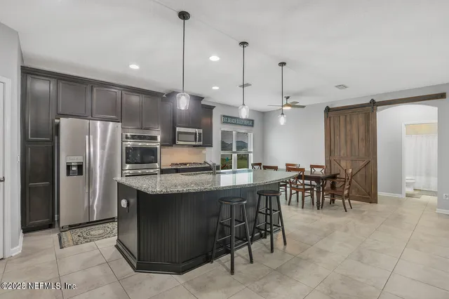 a kitchen with stainless steel appliances kitchen island granite countertop a table a chairs a refrigerator and a sink